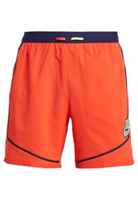 Shorts de sport orange avec une taille bleu marine, présentant un accent vert contrastant et un liseré noir le long des coutures latérales. Panneaux en maille inclus.