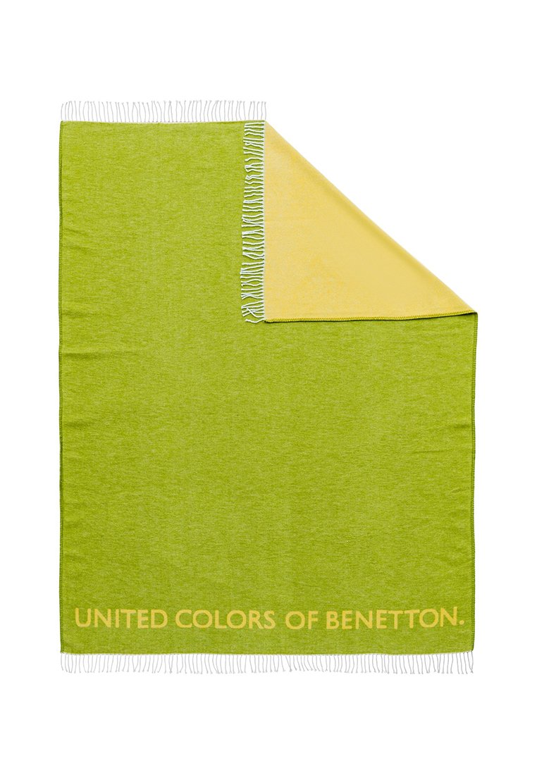 Groene en gele deken met franjes, voorzien van de tekst "UNITED COLORS OF BENETTON" in oranje op de groene zijde. Zachte textuur.