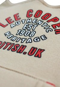 Tissu beige avec texte en noir et rouge vif. Comprend les mots "LEE COOPER", "AUTHENTIC" et "HERITAGE EST 1908", dans différentes tailles et styles.