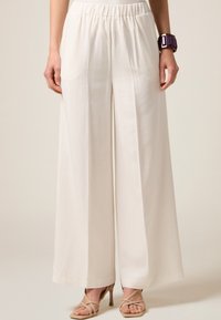 Pantaloni largi, de culoare crem, cu un brâu elastic. Textură netedă, material ușor și două buzunare laterale.