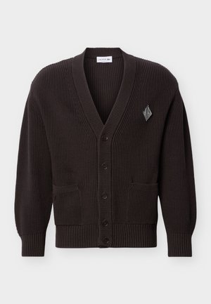 Cardigan en maille côtelée marron foncé avec col en V, boutonné à l'avant, deux poches, et une petite étiquette logo en forme de losange sur le côté gauche de la poitrine.