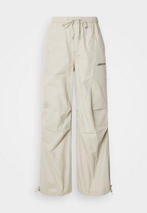Beige, wide-leg trousers made of lightweight fabric. Features an elastic waistband with a drawstring and a printed logo on the side.