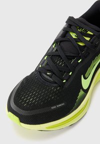 Baskets de course noires Nike avec une tige en mesh, des accents réfléchissants, des détails en néon jaune et une semelle texturée pour l'adhérence et l'amortissement.