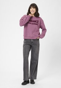 Felpa viola con testo "RADIANCE COSMIC ELEGANCE"; abbinata a jeans neri a vita alta e scarpe chunky nere.