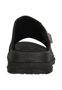 Musta sandaali selkäosattomalla muotoilulla, jossa on kuvioitu kumipohja ja säädettävä hihna istuvuuden varmistamiseksi. Sileä sisävuori, jossa on minimaalista yksityiskohtaisuutta.