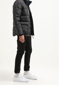 Svart dunjacka med quiltat mönster, dragkedjestängning och sidofickor. Bärs med svarta byxor, vita sneakers och randiga vita strumpor.