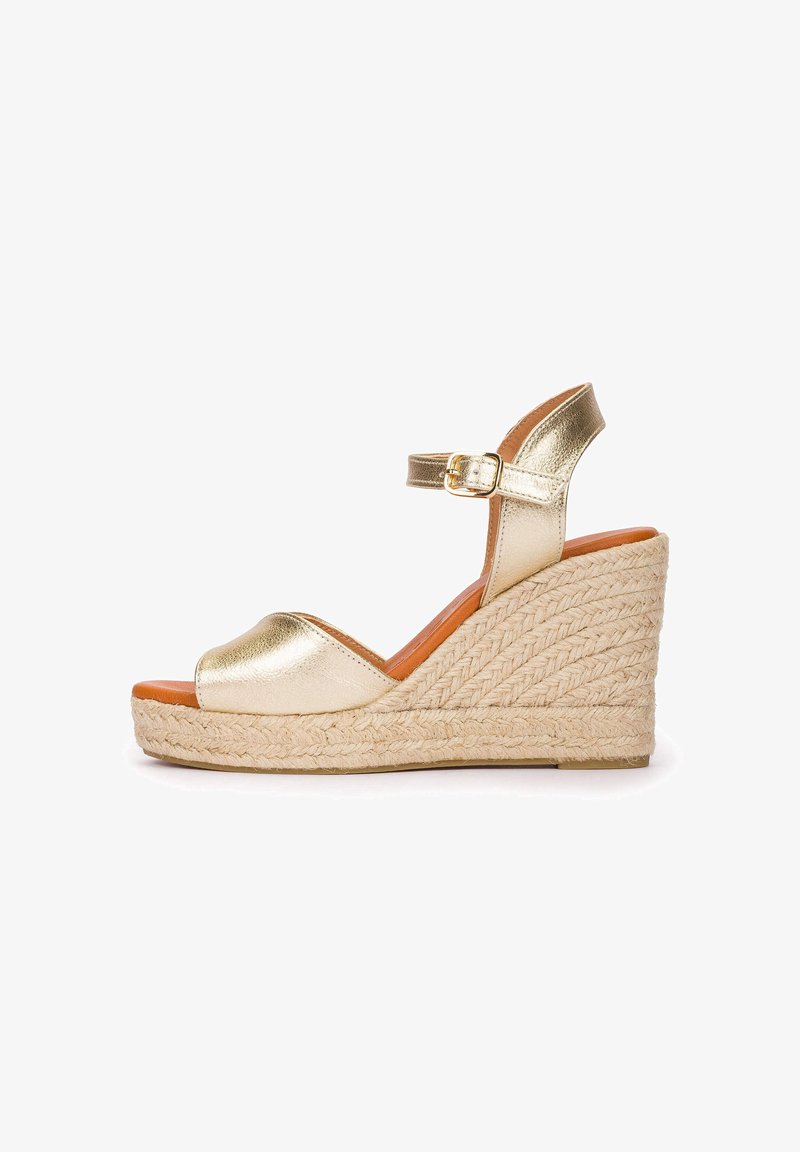 Sandalia de cuña metálica dorada con correa en el tobillo y hebilla, suela plataforma de yute trenzado, puntera abierta y plantilla color coñac, vista lateral sobre fondo blanco.