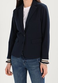 Granatowa marynarka wykonana z miękkiego materiału, z dopasowanym krojem, zapinana na guzik i z paskami na mankietach. Dwie przednie kieszenie.