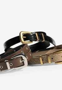 Trīs jostas: melna spīdīga josta ar zelta sprādzi, brūna matēta josta ar sudraba detaļām un gaiši brūna teksturēta josta ar zelta akcentiem.