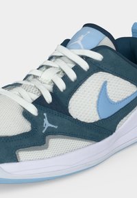 Λευκό και ανοιχτό μπλε αθλητικό παπούτσι με πλεκτό ύφασμα, επενδύσεις από δέρμα σουέτ, λευκά κορδόνια και λογότυπα Jumpman και Nike Swoosh στο πλάι και στη γλώσσα.