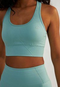 Jasnoniebieski stanik sportowy z teksturowanymi wzorami, z logo w kształcie serca. Wykonany z elastycznej tkaniny, ma dopasowany krój i żeberkowe akcenty.