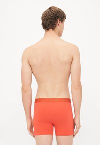 Red cotton boxer briefs with a gold Nike logo on the elastic waistband. Fitted design with short legs and a smooth texture.