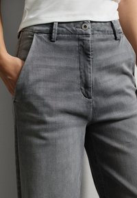 Grijze katoenen broeken met een gladde textuur, voorzien van een voorzak en een metalen knoopsluiting. Slim fit met minimale stikseldetails.
