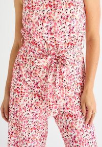 Floral jumpsuit in lightweight fabric features a pink and white pattern with black accents. Includes a tie waist detail for a fitted look.