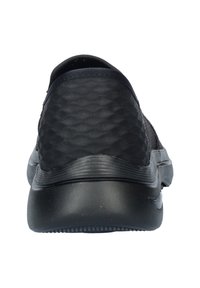 Zwarte instapper met een gestructureerde bovenkant, een gladde zwarte zool en een ronde hak zonder zichtbare veters of sluitingen.