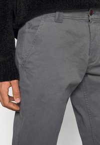 Grijze katoenen broek met een klassiek ontwerp, voorzien van zijzakken en subtiele stiksel details. De stof heeft een gladde, matte afwerking.