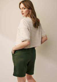 Skåret, lyst stribet top med korte ærmer, parret med grønne linned shorts med sidelommer og elastisk talje.