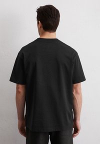 Zwarte katoenen t-shirt met korte mouwen, ronde hals en een ontspannen pasvorm. Naadloos achterdesign, minimale accentdetails.