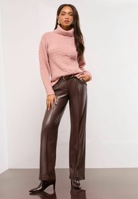Hellblauer, kabelgestrickter Rollkragenpullover, kombiniert mit hochgeschnittenen, braunen, ledernen weit geschnittenen Hosen und spitzen, braunen Stiefeletten mit Absatz.