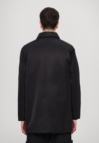 Black, lightweight outerwear jacket with a classic collar, long sleeves, and a straight cut. Smooth texture with a clean, minimal design.