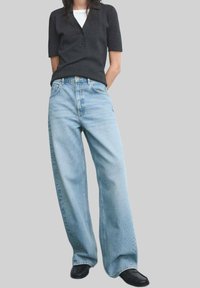 Donkergrijs poloshirt met korte mouwen, lichtblauwe wijde jeans en zwarte schoenen. De jeans hebben een klassiek vijfzakkenontwerp en een lichte wassing.