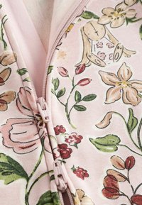 Rosa blumige Stoffjacke mit bunten Mustern, die Blumen und ein Kaninchenmotiv zeigt, strukturiert, mit einem leichten Reißverschluss in der Mitte.