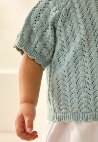 Himmelblauer, gestrickter Kurzarm-Top mit gewelltem Saum, der ein strukturiertes Muster aus Löchern und kleinen Blättern aufweist.