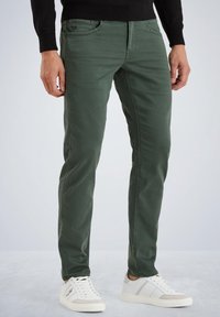 Jeans de mezcla de algodón verde con corte slim, que cuentan con cinco bolsillos y costuras sutiles. Combinados con zapatillas blancas.