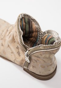 Bottine beige avec motif de dentelle florale, fermeture éclair argentée et doublure texturée à rayures vertes, orange et brunes. Modèle à semelle plate.