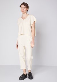 Cremefarvet loungewear sæt med en løs pasform, kortærmet V-hals top med en brystlomme og matchende smalnede bukser.