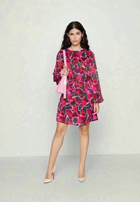 Vestido colorido com um padrão floral em rosa, vermelho e verde. Mangas longas e um design com cintura ajustada, combinado com uma bolsa rosa.