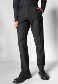 Pantalons noirs en tissu lisse, dotés d'une coupe sur mesure, de plis marqués et de poches. Assortis à des chaussures en cuir noires unies.