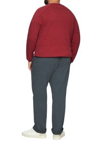 Rode gebreide trui met lange mouwen, gecombineerd met losse donkergrijze broeken en witte sneakers. Weergave van de achterkant.