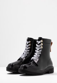 Bottines en cuir verni noir avec une semelle en caoutchouc, dotées de lacets antidérapants imprimés "See by Chloé" et d'œillets dorés.