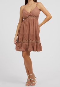 Hněd dress z lnu s tenkými ramínky, vrstveným lemem, vyšívanými akcenty a uvolněným střihem, doplněné o stříbrné sandály na řemínkách.