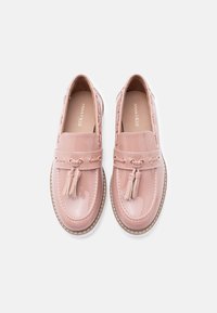 Paire de mocassins pour femmes d'un rose pâle brillant avec des glands et des détails de coutures, vue de dessus sur un fond blanc.