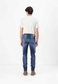 Στενές μπλε τζιν με διακριτική φθορά, συνδυασμένες με γκρίζα μπλούζα. Εντυπωσιακή δερμάτινη ετικέτα στη μέση πίσω πλευρά.