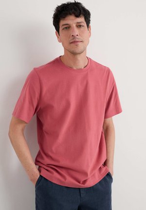 T-shirt a maniche corte con scollo rotondo in corallo tenue, realizzato in cotone morbido. Vestibilità rilassata con una texture liscia, abbinato a pantaloni corti blu navy.