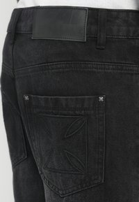 Fekete farmernadrág texturált hátsó folttal, látható varrással és hímzett mintával a hátsó zseben.