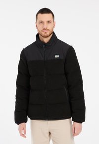Sort fleece puffer-jakke med lynlås, der har en glat sort øverste del og en tekstureret nederste del. Ribbet manchetter og talje medfølger.