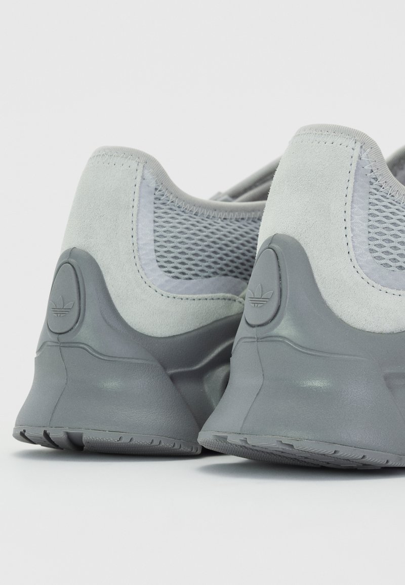 Graue Sportschuhe aus einer Mischung von Wildleder und Mesh-Materialien, mit einem abgerundeten Absatz und geprägtem Logo auf der Ferse. Gummisohle.