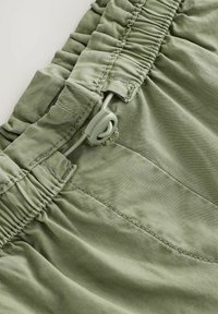 Primo piano di tessuto verde oliva con cintura elastica e coulisse regolabile con fermaglio in plastica per stringere.