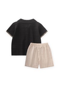 Completo a due pezzi composto da una maglietta nera a maniche corte con colletto e pantaloni corti beige a righe con vita elasticizzata.