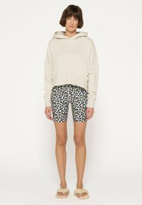 Lys grå kort hoodie med en bred hals, parret med sort og gul leopardmønstret cykelshorts og beige fluffy slippers.