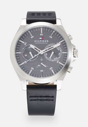 Montre chronographe avec un bracelet en cuir noir, un boîtier en acier inoxydable argenté et un cadran texturé gris foncé avec trois sous-cadrans et des marqueurs luminescents.