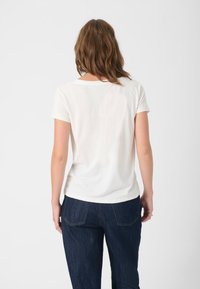 T-shirt blanc à manches courtes avec un col rond, texture lisse, associé à un jean en denim bleu foncé avec des poches arrière.