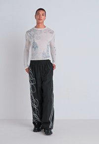 Long-sleeve, sheer white top with blue architectural print; loose black pants with white abstract line patterns; worn with black shoes.