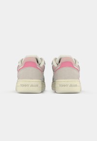 Een paar beige en roze sneakers gezien vanaf de achterkant, met "Tommy Jeans" in reliëf op de crèmekleurige zolen.