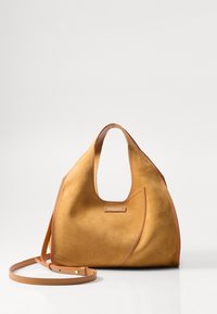 Sac à main en daim beige avec une silhouette incurvée, une anse découpée et des coutures contrastées. Comprend une bandoulière amovible pour un port polyvalent.