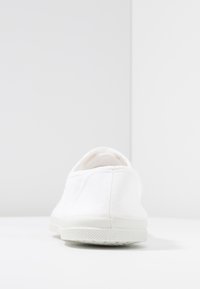 Sneaker bianco in tela con profilo basso, suola in gomma testurizzata, vista posteriore, e superficie liscia senza motivi o accenti visibili.